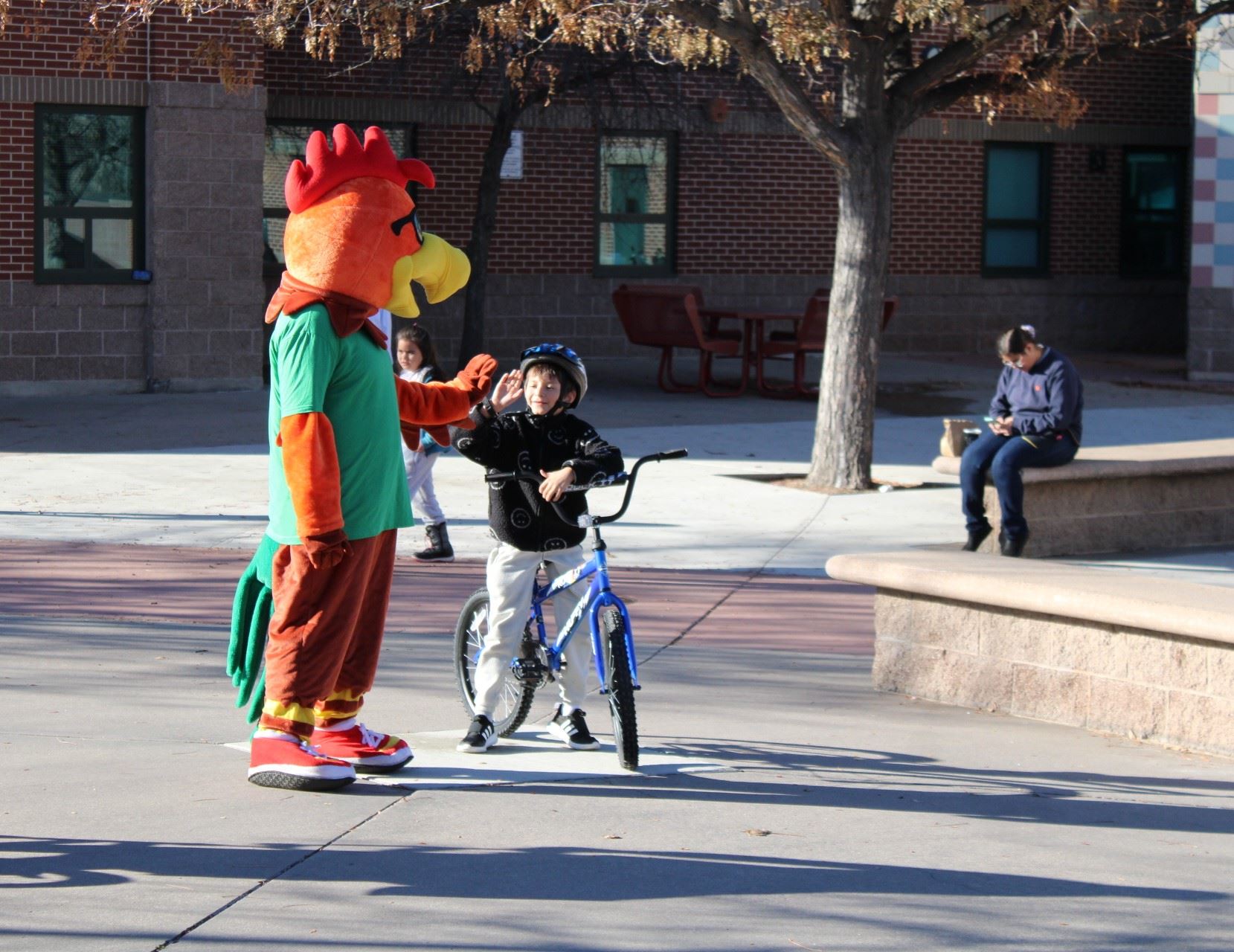 Wheat Ridge Parks and Recreation Booster the Rooster high fiving a child on a bike